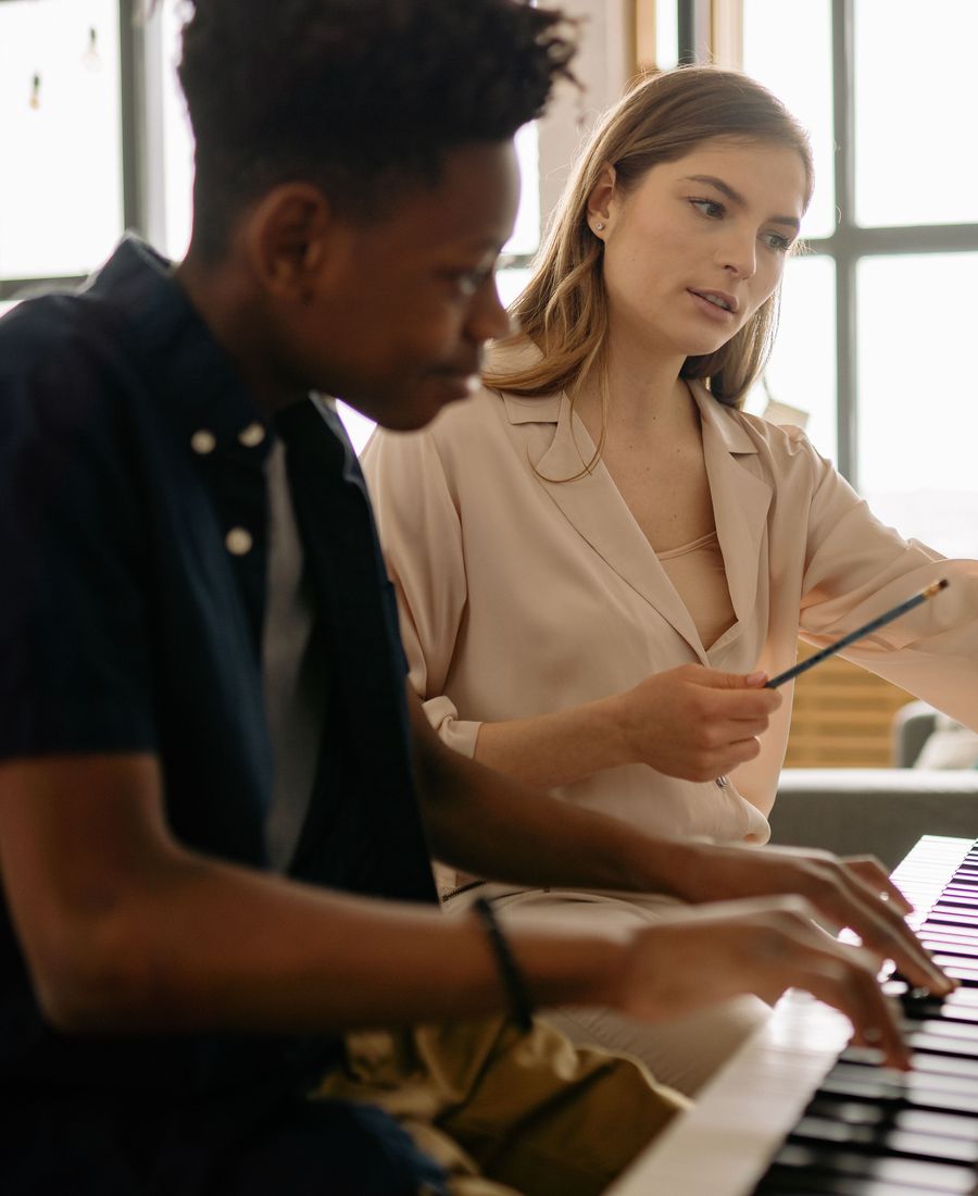 A tutor guiding a student through sheet music at a keyboard during a lesson